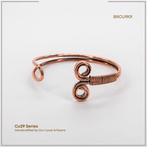May include: A copper-colored bracelet with a unique design. The bracelet features a coiled design on one end and a wrapped wire section. The text "BRCU1901" is visible. The text "Cu29 Series Handcrafted by Our Local Artisans" is also visible.