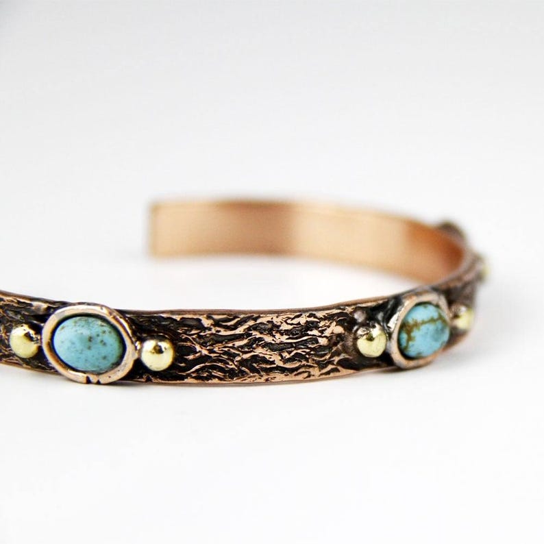 May include: A copper bracelet with a textured surface and turquoise stones. The bracelet has a hammered finish and is accented with gold beads.