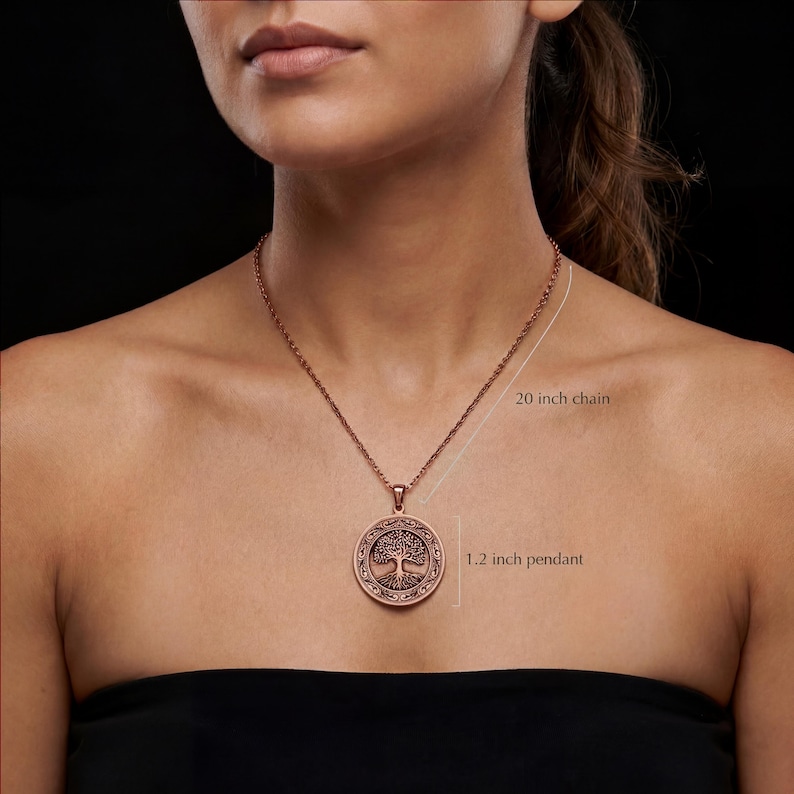 K&ouml;nnte beinhalten: Kupferfarbene Halskette mit einer 50.8 cm langen Kette und einem 3 cm Anh&auml;nger. Der Anh&auml;nger zeigt ein detailliertes Lebensbaum-Design in einem kreisf&ouml;rmigen Rahmen. Die Halskette wird vor dunklem Hintergrund getragen.