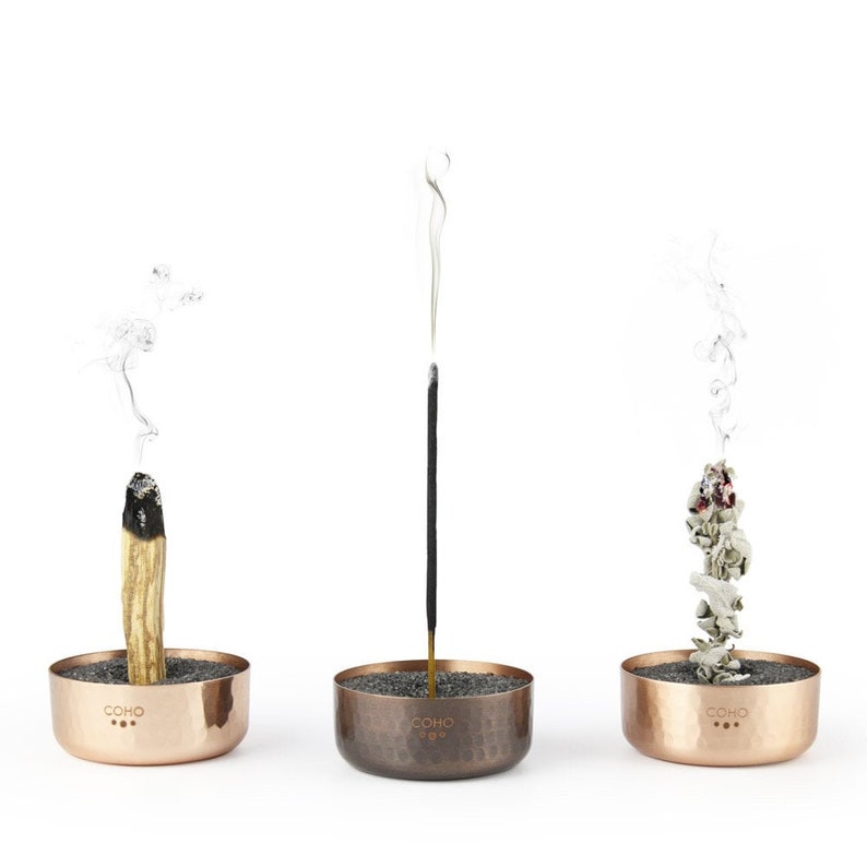 May include: Three copper incense holders with different types of incense burning. The holders are hammered copper and have the word "COHO" engraved on the front.