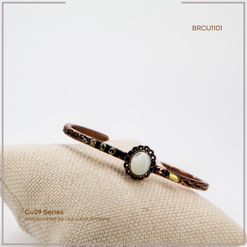 Pu&ograve; includere: Bracciale a polsino color rame con una pietra centrale ovale bianco sporco e un design traforato decorativo. Fa parte della serie Cu29, realizzato a mano da artigiani locali. &Egrave; visibile anche il testo "BRCU1101".