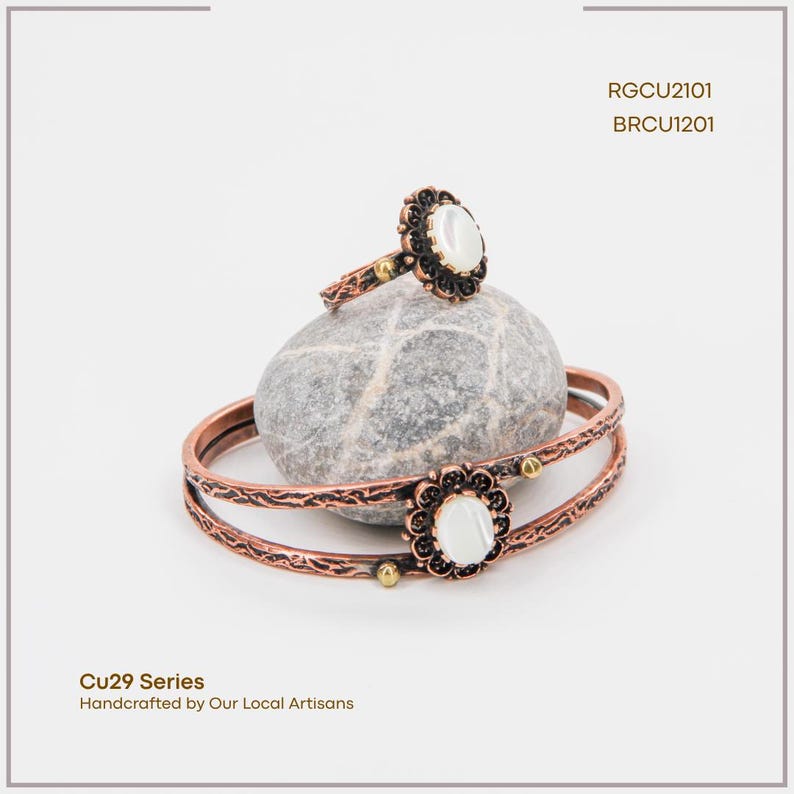 Puede incluir: Un conjunto de anillo y pulsera en tono cobre con un dise&ntilde;o floral y una piedra central blanca de forma ovalada. La pulsera es un brazalete de doble banda. El anillo y la pulsera se exhiben sobre una piedra gris. El texto "Cu29 Series Handcrafted by Our Local Artisans" es visible.