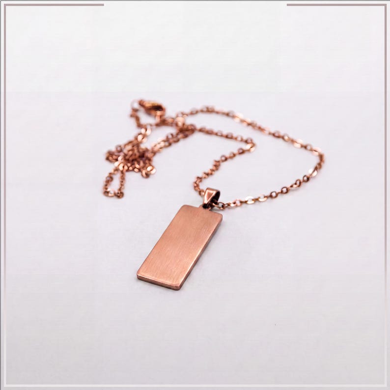 Puede incluir: Un collar de tono oro rosa con un colgante rectangular de acabado met&aacute;lico cepillado. El colgante est&aacute; unido a una delicada cadena a juego del mismo tono, formada por peque&ntilde;os eslabones ovalados uniformes de dise&ntilde;o sencillo y limpio.