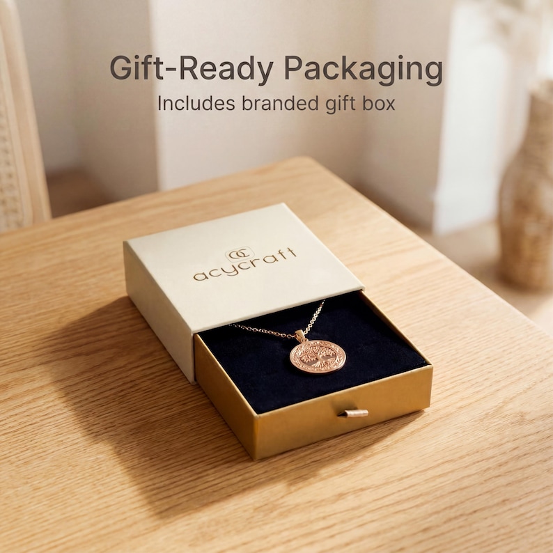 K&ouml;nnte beinhalten: Eine goldene Halskette mit einem runden Anh&auml;nger mit einem Baumdesign, pr&auml;sentiert in einer Geschenkbox. Die beige Box hat einen goldenen Boden und ein dunkelblaues Innere. Der Text "Gift-Ready Packaging" ist sichtbar.