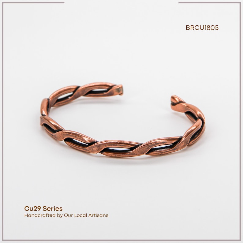 K&ouml;nnte beinhalten: Ein kupferfarbenes Armband mit geflochtenem Design. Das offene Armband besteht aus ineinander verschlungenen Metallstr&auml;ngen. Der Text "BRCU1805" befindet sich in der oberen rechten Ecke. Der Text "Cu29 Series Handcrafted by Our Local Artisans" befindet sich in der unteren linken Ecke.