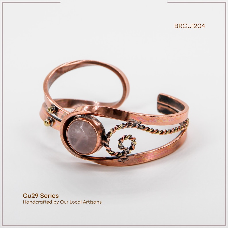 May include: Copper cuff bracelet with a light pink gemstone center. The bracelet features a twisted rope design and small gold-colored accents. The text "BRCU1204" is visible. The text "Cu29 Series Handcrafted by Our Local Artisans" is also visible.