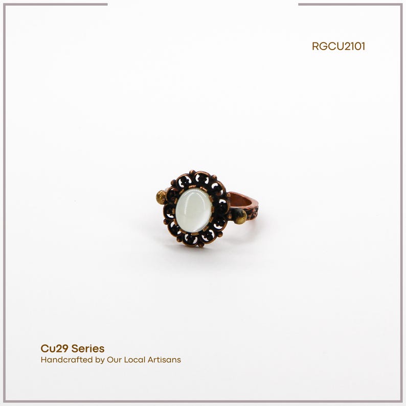 Puede incluir: Un anillo de tono cobrizo con una piedra ovalada blanquecina en el centro, rodeada por un dise&ntilde;o de filigrana oscura. El anillo presenta peque&ntilde;os detalles decorativos en la banda. El texto "Cu29 Series Handcrafted by Our Local Artisans" es visible.