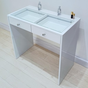 May include: White vanity table with two drawers and a glass top. The top has two compartments for storage. The table has silver drawer pulls.