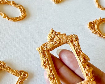 May include: A set of five gold-colored ornate picture frames with intricate details. The frames are various sizes and shapes, including oval, rectangular, and square.