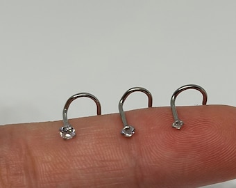 May include: Three silver nose rings with clear rhinestones. The rings are displayed on a finger.