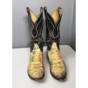 May include: A pair of cowboy boots. The boots have a snakeskin foot and black leather upper with decorative stitching. The interior is a light tan colour. The boots have a pointed toe.