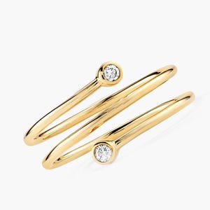 May include: A gold ring with a spiral design. The ring has two small, round, clear gemstones set in the gold. The ring's design is modern and minimalist, with a polished finish.