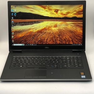 以下が含まれることがあります： 黄色とオレンジ色の空の風景画像を表示する、大きな画面を備えた黒いDellラップトップ。 ラップトップには、フルキーボード、タッチパッド、指紋リーダーが搭載されています。 Dellのロゴが見えます。