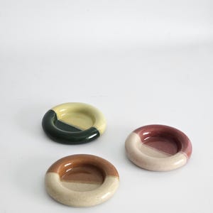 May include: A set of three ceramic mugs with a speckled, matte finish. The mugs are in shades of cream, light gray, and dark gray. Each mug has a simple, modern design and a rounded handle. Perfect for coffee or tea.