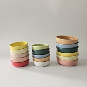 May include: A set of colorful ceramic bowls stacked in three groups. The bowls are in various shades of yellow, pink, red, green, blue, and beige.