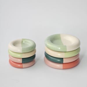 May include: Stacks of ceramic coasters in various colors, including green, pink, and cream. Each coaster is divided into two color sections. The coasters are arranged in two stacks, with one stack slightly smaller than the other.
