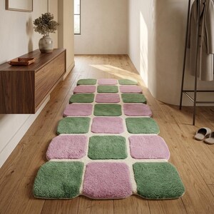 May include: A rectangular rug featuring a repeating pattern of green and pink squares. The rug is positioned on a wooden floor in a hallway. The rug's design presents a modern, geometric pattern.
