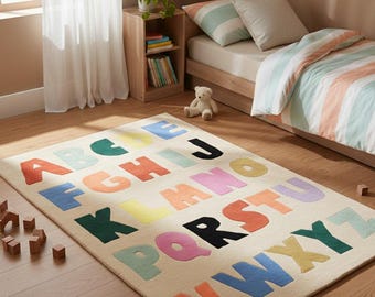 May include: A colourful alphabet rug in a child's bedroom. The rug features letters in various colours on a beige background. The room includes a bed, books, and a teddy bear. The rug measures approximately 152 cm long and 102 cm wide.
