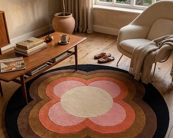 Puede incluir: Una alfombra redonda de estilo retro con un diseño floral. La alfombra presenta un borde exterior negro, seguido de capas de marrón, naranja, rosa y un centro beige. La alfombra está colocada sobre un suelo de madera en un salón.