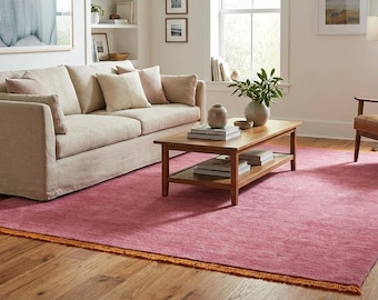 Puede incluir: Un salón con un gran sofá beige y una alfombra rosa con flecos naranjas. También hay una mesa de centro de madera y un sillón de cuero. La alfombra, de unos 200 cm x 300 cm, añade un toque de color a la habitación.