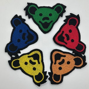 May include: Five colorful embroidered patches featuring a bear with a smiling face. The bears are green, blue, red, yellow, and orange.