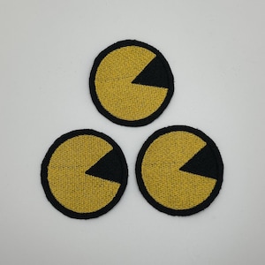 以下が含まれることがあります： パックマンのキャラクターが描かれた、黄色と黒の刺繍入りアイロン接着パッチが3つです。
