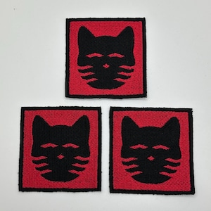 Op de afbeelding: Drie vierkante patches met een zwart kattengezicht op een rode achtergrond. Het kattengezicht heeft een eenvoudig, gestileerd ontwerp met puntige oren en snorharen. De patches zijn waarschijnlijk voor kleding of accessoires.