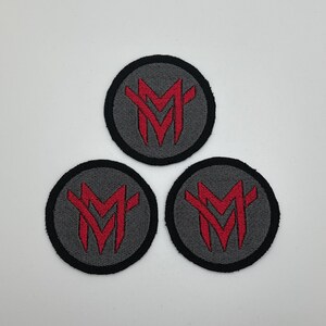 May include: Three gray and black circular patches with a red stylized letter "M" in the center.