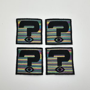 May include: Four square patches with a black question mark and an eye on a rainbow striped background.