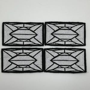 May include: Four rectangular patches with a geometric design. Each patch has a black border and a white interior with a black, symmetrical pattern. The patches are arranged in a two-by-two grid on a white background.
