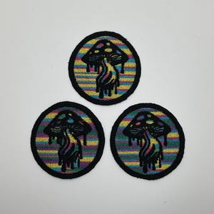 May include: Three round embroidered patches with a black mushroom design on a rainbow striped background.