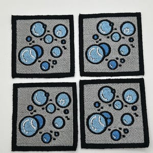May include: Four gray square patches with black borders, each featuring a design of blue and white bubbles on a gray background.