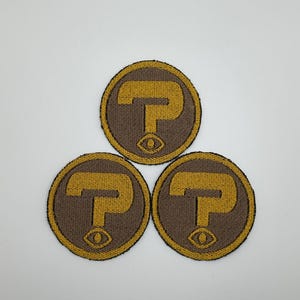 May include: Three brown and gold embroidered patches with a stylized letter "P" and an eye symbol.