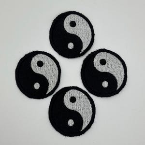 May include: Four circular patches featuring the yin and yang symbol. Each patch has a black background with a white, textured, curved shape and a small white dot. The patches are arranged in a square pattern.