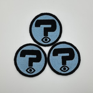 May include: Three blue and black embroidered patches with a question mark and an eye design.