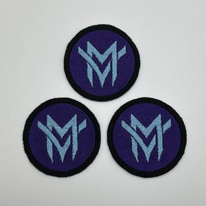May include: Three purple and black embroidered patches with a light blue stylized letter "M" design.