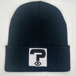 May include: Black beanie with a white square patch featuring a black question mark with an eye inside.