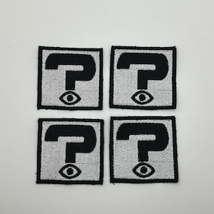 May include: Four black and white embroidered patches with a question mark and an eye design. The patches are square and have a black border.