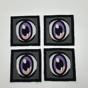 May include: Four embroidered iron-on patches featuring a stylized purple eye with a white iris and pink pupil, each eye is set within a black square with a gray background.