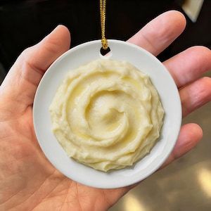 Peut inclure: Un ornement rond en céramique blanche présentant un graphique réaliste et texturé de purée de pommes de terre en spirale avec une finition brillante. L'ornement possède un petit trou en haut pour le suspendre et inclut un cordon doré fin.