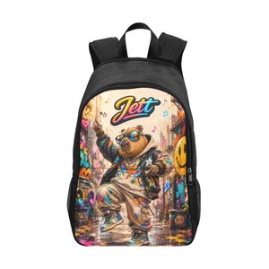 May include: Black backpack featuring a colorful illustration of a bear wearing sunglasses and a hoodie, dancing in a graffiti-filled urban setting. The name "Jett" is written in a stylized font above the bear. The backpack has black straps and side pockets.