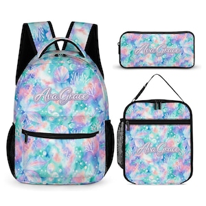 Peut inclure: Un ensemble comprenant un sac à dos, une trousse et un sac à déjeuner. L'ensemble présente un motif aquarelle avec des coquillages, du corail et le nom "Ava Grace" en écriture cursive. La palette de couleurs comprend des nuances de bleu, de rose et de violet.