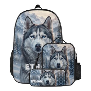 May include: A backpack, lunch bag, and pencil case set featuring a printed image of a Siberian husky with blue eyes against a snowy mountain forest background. The name ETHAN is printed in white block letters on each of the three items.