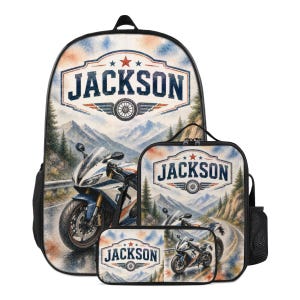 Op de afbeelding: Een set bestaande uit een rugzak, lunchtas en etui met een afbeelding van een motorfiets op een bergweg. Elk item toont de naam JACKSON in een blauw embleem met een rode ster en wielpictogram tegen een aquarelachtig berglandschap.
