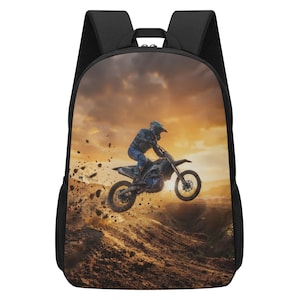 May include: A black backpack featuring a printed graphic of a motocross rider jumping a dirt bike over a mound of earth. The scene is set against a golden sunset sky with flying dirt particles and a rugged terrain background.