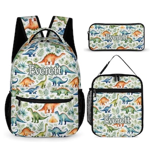 May include: A backpack, a rectangular pencil case, and a lunch bag, all featuring a white background with a repeating pattern of green tropical leaves and colourful dinosaurs. Each item displays the name Everett in a grey serif font.