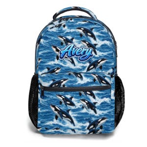 Puede incluir: Mochila azul con un estampado de orcas nadando en olas del océano. La mochila tiene un bolsillo lateral de malla negra y un bolsillo frontal. El nombre "Avery" está escrito en azul en la parte delantera.