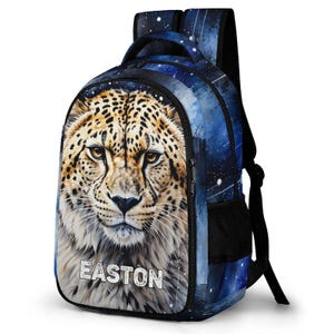 May include: A backpack featuring a galaxy-themed blue and black background with a large, detailed leopard face printed on the front pocket. The name EASTON is printed in white, distressed capital letters below the leopard's chin. It has black straps.