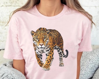 Puede incluir: Camiseta rosa claro con una ilustración detallada de un jaguar. El jaguar se representa con su distintivo pelaje manchado en tonos marrones y negros, con una expresión concentrada. El diseño está centrado en la camiseta.