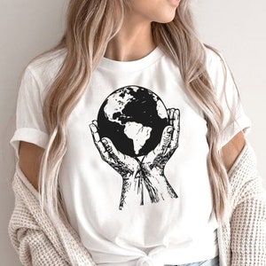 May include: White t-shirt with a black and white illustration of hands holding a globe.